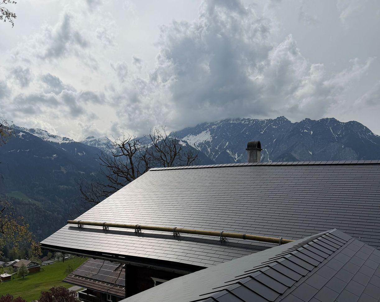 Dach mit grauen Schindeln vor bewölktem Himmel und Bergpanorama